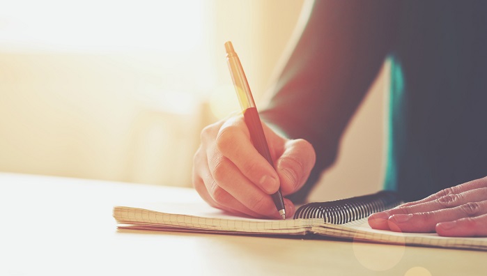 women with pen writing on notebook