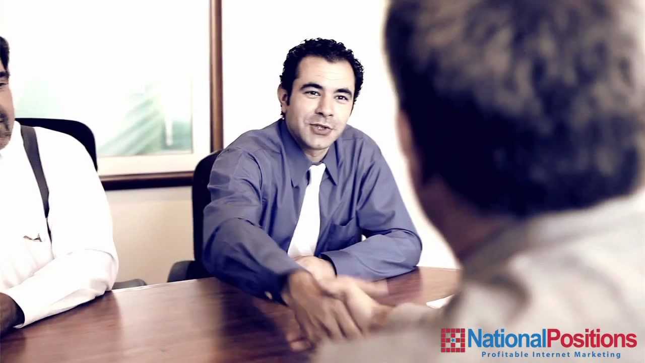 A man in a blue shirt and white tie shakes hands with someone across a table in a conference room. The logo "National Positions Profitable Internet Marketing" is visible in the bottom right corner.