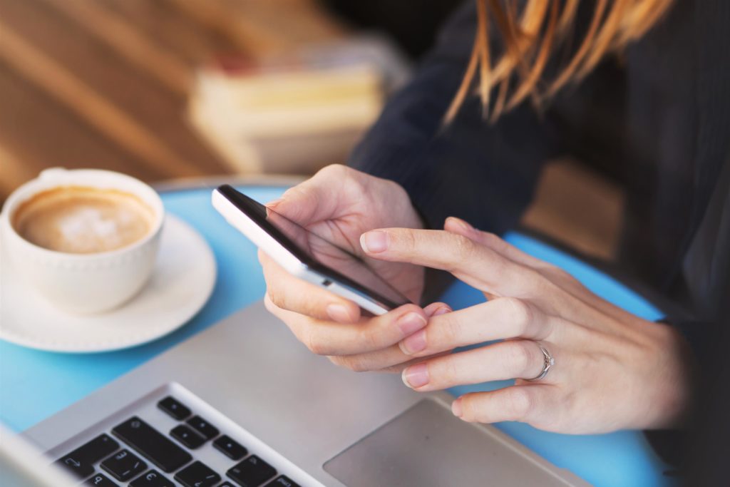 woman's hands searching mobile with coffee in cafe
