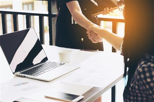 Two women shaking hands across a desk