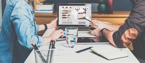 Two people sitting at monitor looking at charts on screen