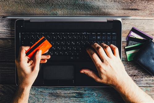 Man's hands over keyboard holding orange credit card