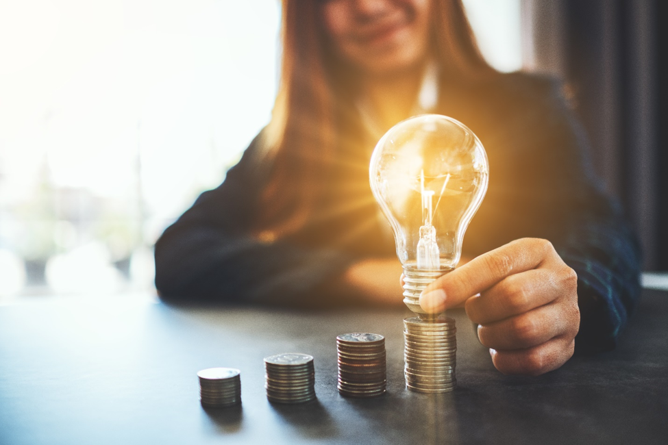 woman illuminating light bulb that is on top of a stack of quarters