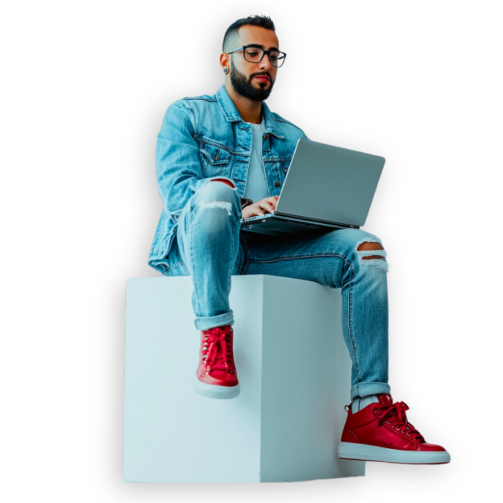 A person wearing denim and red sneakers sits on a white cube, typing on a laptop while brainstorming a marketing strategy.