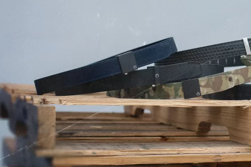Four Nexbelt styles—black, textured black, camouflage, and olive green—are displayed on a stack of wooden pallets against a plain background.