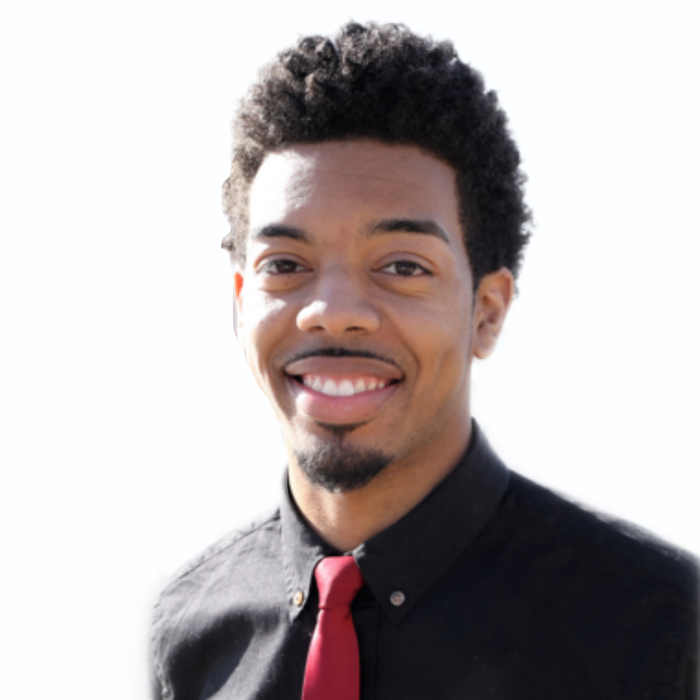 Meet The Team: A man with short curly hair wearing a black shirt and red tie smiles at the camera against a white background.